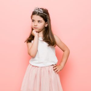 Little girl wearing a princess look looking sideways with doubtful and skeptical expression.